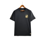 Black short-sleeve T-shirt on a wooden hanger with a gold crest logo on the left chest and two small stars above it.