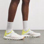 White running shoes with yellow heel accents and cloud-like segmented sole, worn with white crew socks.