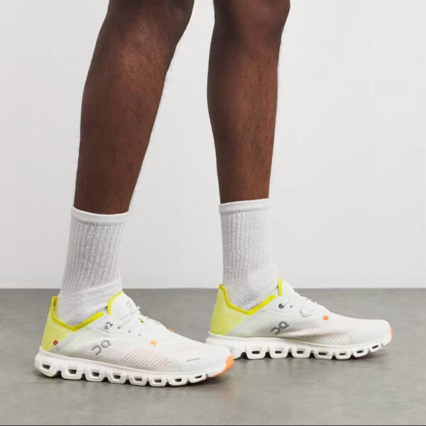 White running shoes with yellow heel accents and cloud-like segmented sole, worn with white crew socks.