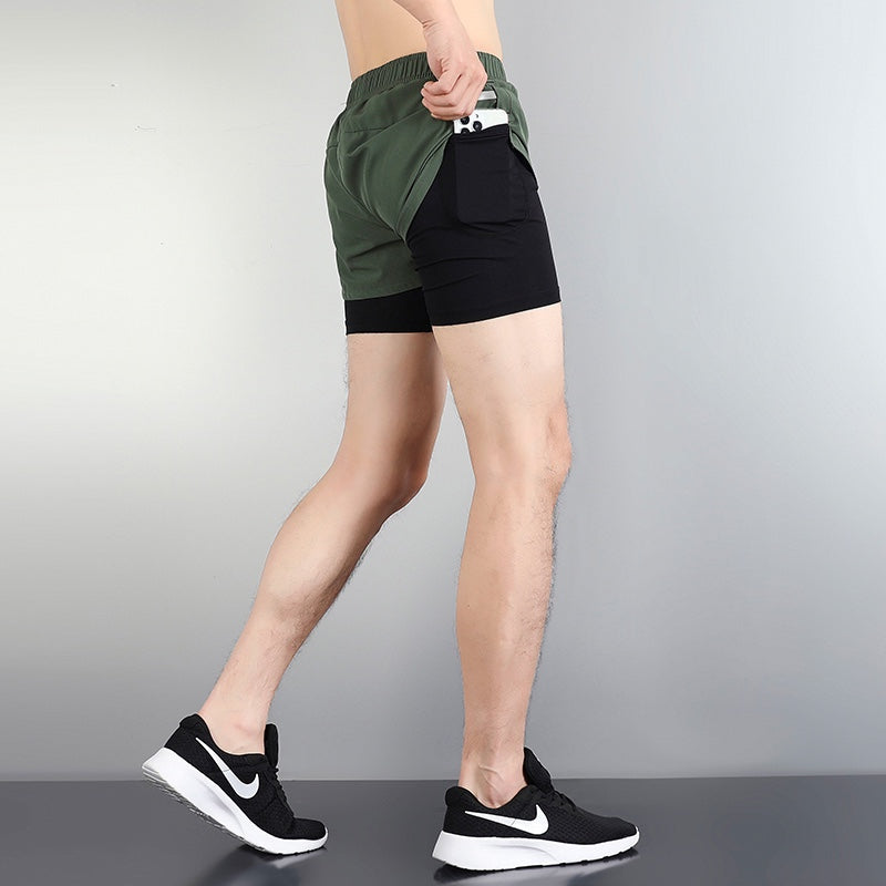 17cd481a | UAE SPORT STORE Side view of a person in green athletic shorts over black compression shorts, with a smartphone visible in the back pocket, wearing black Nike sneakers.