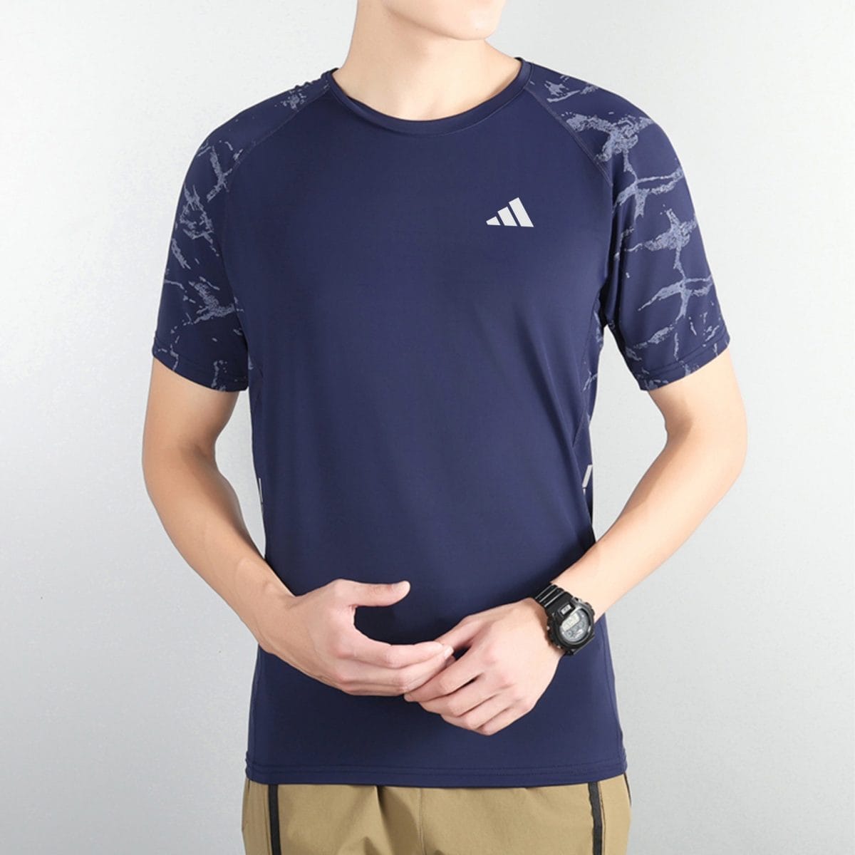Navy athletic rash guard with a white logo on the chest and patterned sleeves, paired with beige shorts and a wristwatch visible on the left wrist.