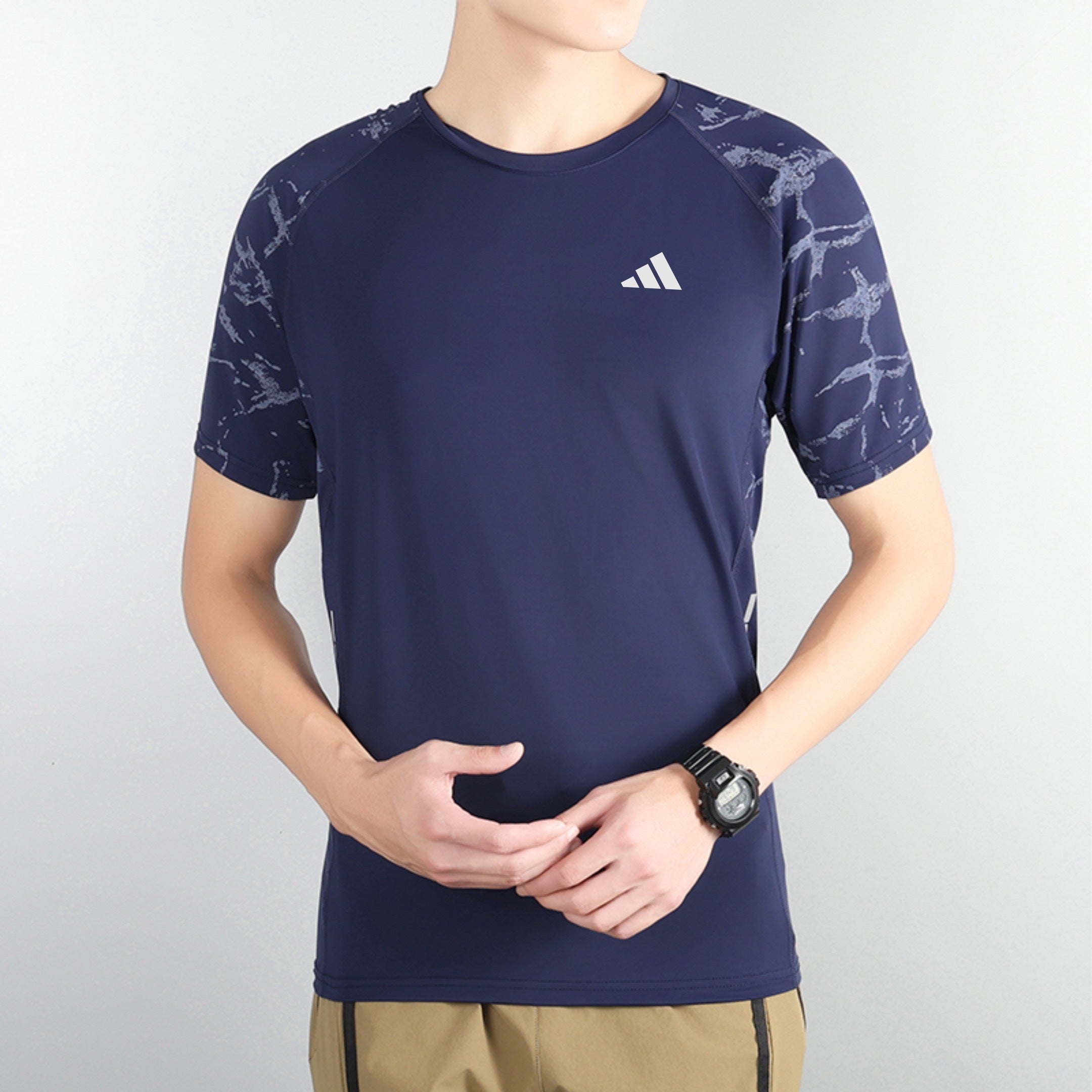 180e5dbf | UAE SPORT STORE Navy athletic rash guard with a white logo on the chest and patterned sleeves, paired with beige shorts and a wristwatch visible on the left wrist.