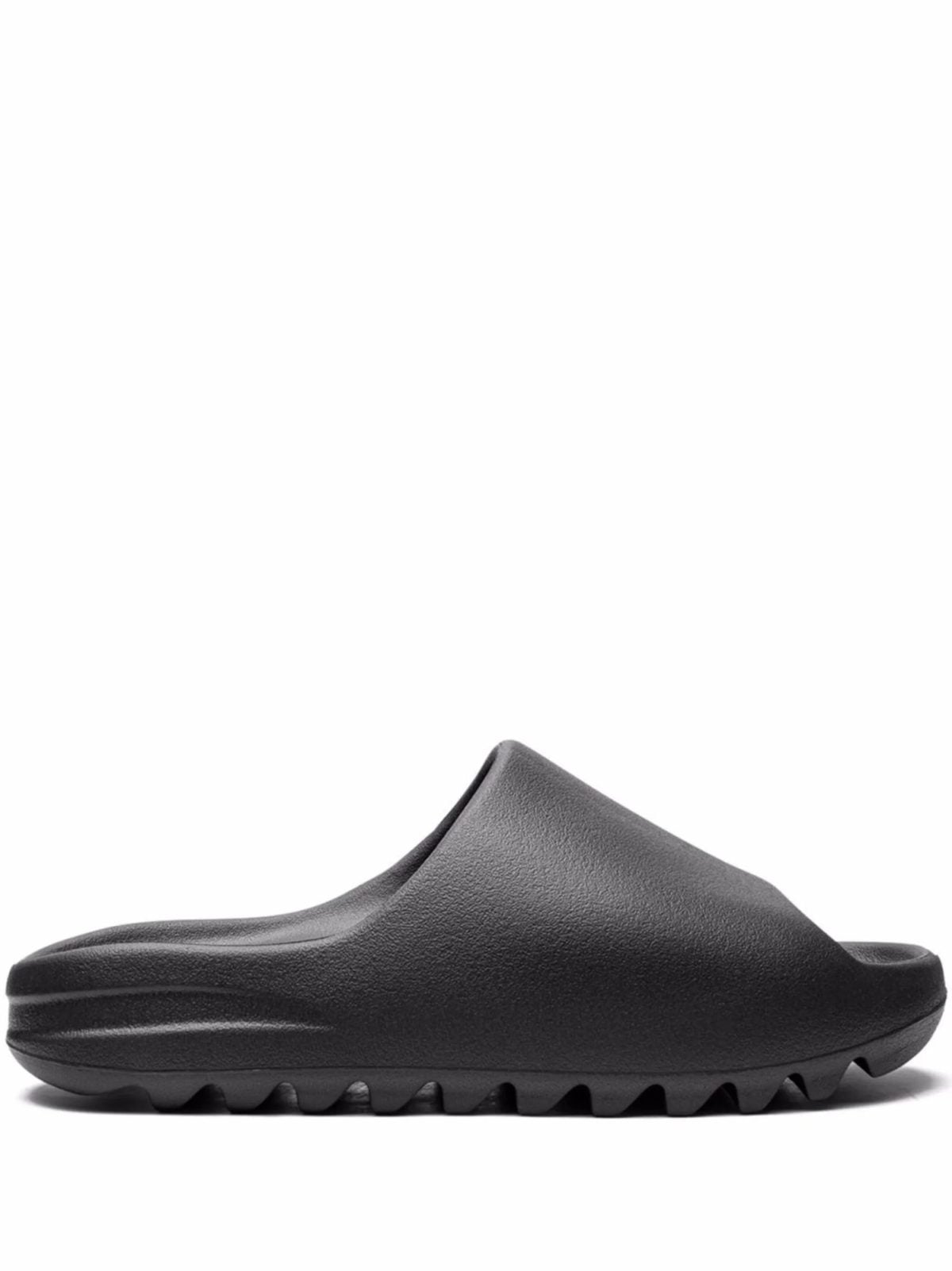 Black slip-on sandal with a textured strap and grooved sole, shown from the side on a white background.