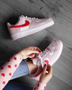 Hands tying pink and white Nike sneakers on a wooden floor, with another shoe nearby.