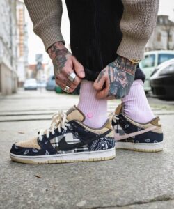 Close-up of tattooed hands tying pastel pink socks over patterned sneakers on a city sidewalk.