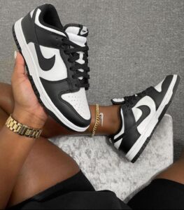 Two black-and-white Nike sneakers with white soles, held by a person wearing a gold watch and bracelet.