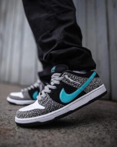Athletic sneaker with a turquoise swoosh, black panels, and gray laces on a concrete surface.