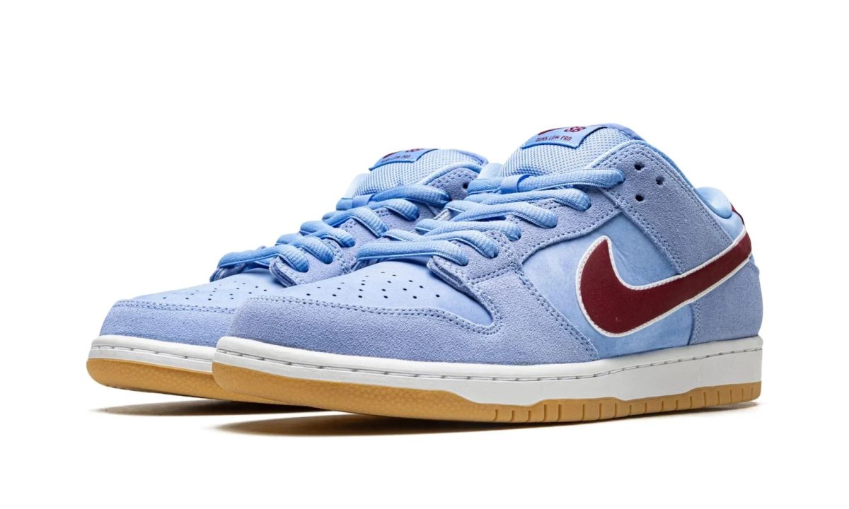 Close-up of light blue suede sneakers with blue laces, white midsole, and red swoosh seen from the side/toe area.
