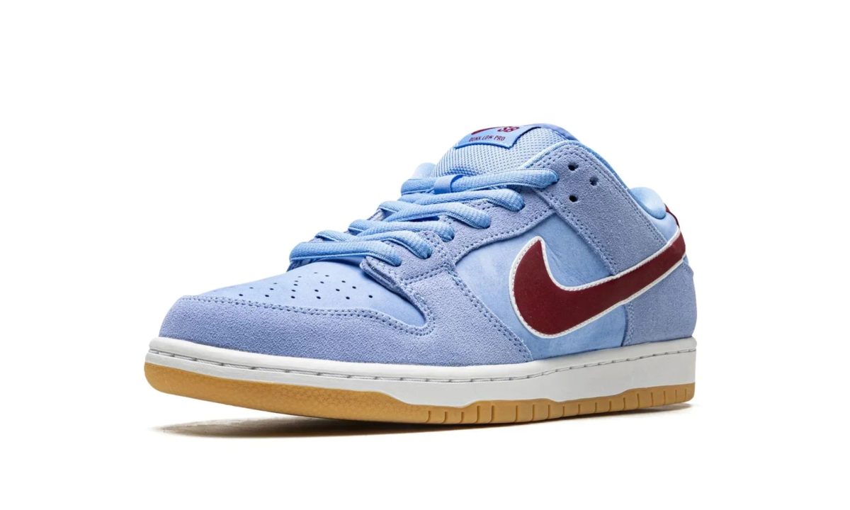 Light blue suede sneaker with a red swoosh, white midsole, and gum outsole photographed from a low front-left angle on a white background.