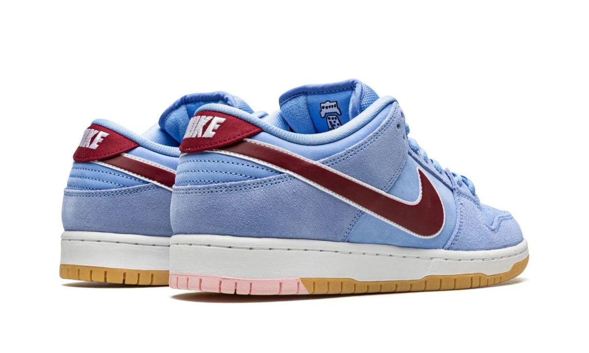 Blue Nike sneakers in suede with a red Swoosh, light blue upper, and a multi-tone outsole (gum, pink) visible at the bottom.