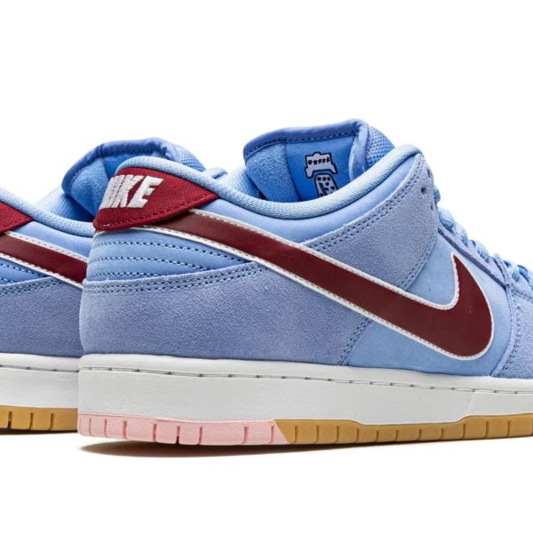 Blue Nike sneakers in suede with a red Swoosh, light blue upper, and a multi-tone outsole (gum, pink) visible at the bottom.