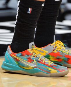 Colorful Nike basketball shoes with turquoise sole and yellow laces worn with black NBA socks on a wood gym floor
