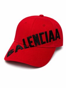 Red baseball cap with a black embroidered BALENCIAGA logo across the front, curved brim visible