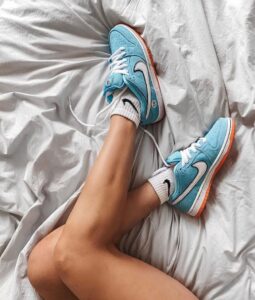 Legs crossed on a gray sheet, wearing turquoise sneakers with white laces and orange soles.