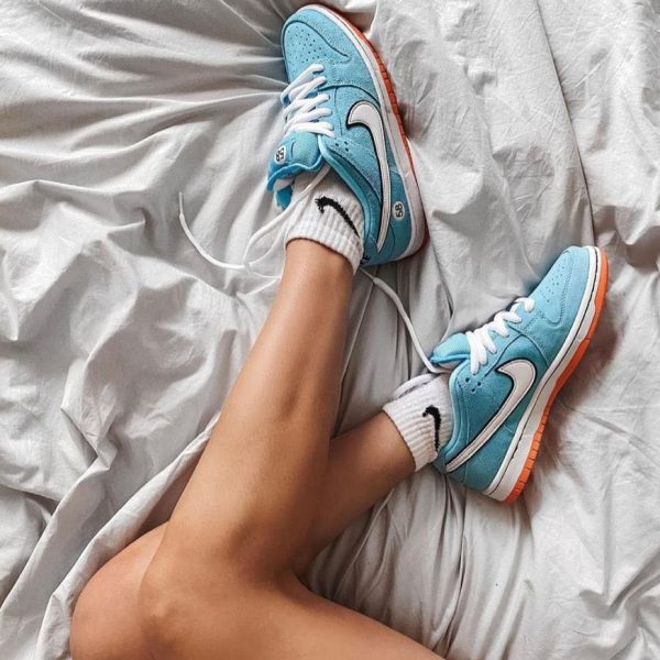 Legs crossed on a gray sheet, wearing turquoise sneakers with white laces and orange soles.