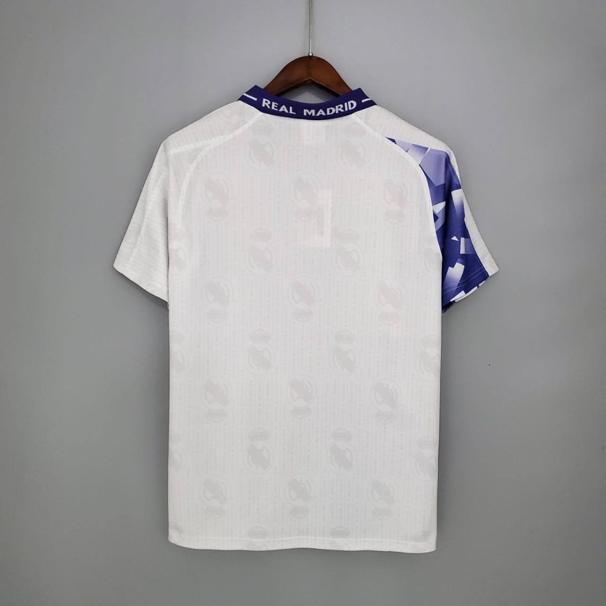 White Real Madrid football jersey hanging on a wooden hanger, back view, purple collar reading REAL MADRID.