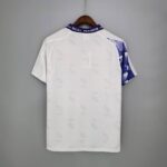 White Real Madrid football jersey hanging on a wooden hanger, back view, purple collar reading REAL MADRID.