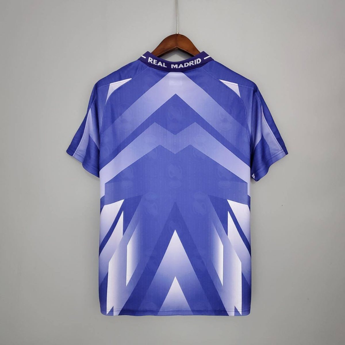 Blue and white chevron-pattern sports jersey hanging on a wooden hanger, collar reads Real Madrid.