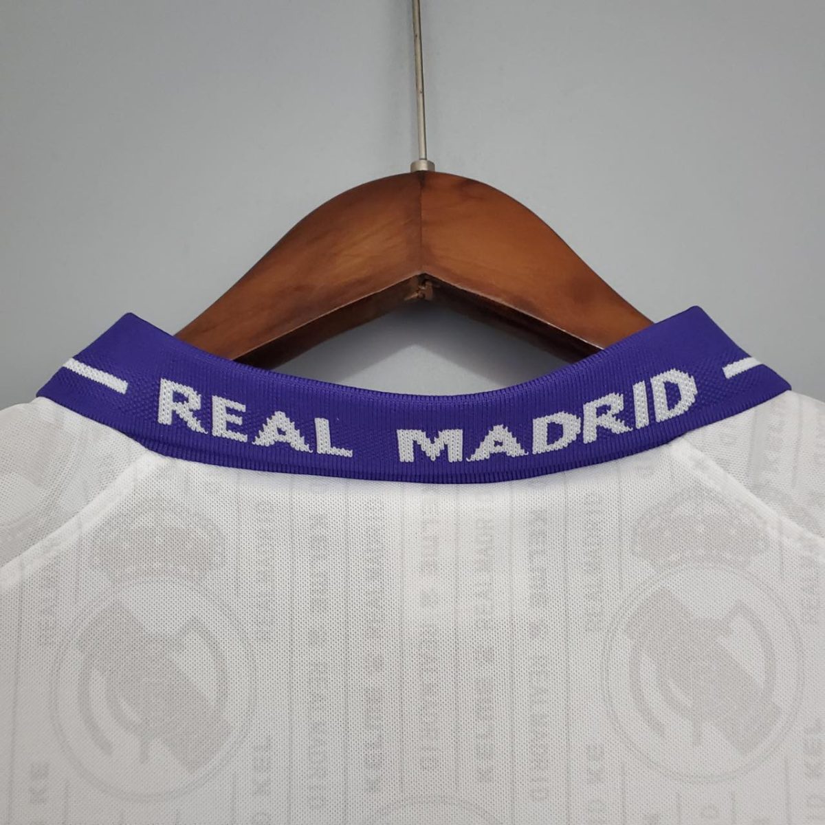 White Real Madrid football jersey on a wooden hanger, focusing on the purple collar with REAL MADRID text.