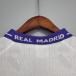 White Real Madrid football jersey on a wooden hanger, focusing on the purple collar with REAL MADRID text.