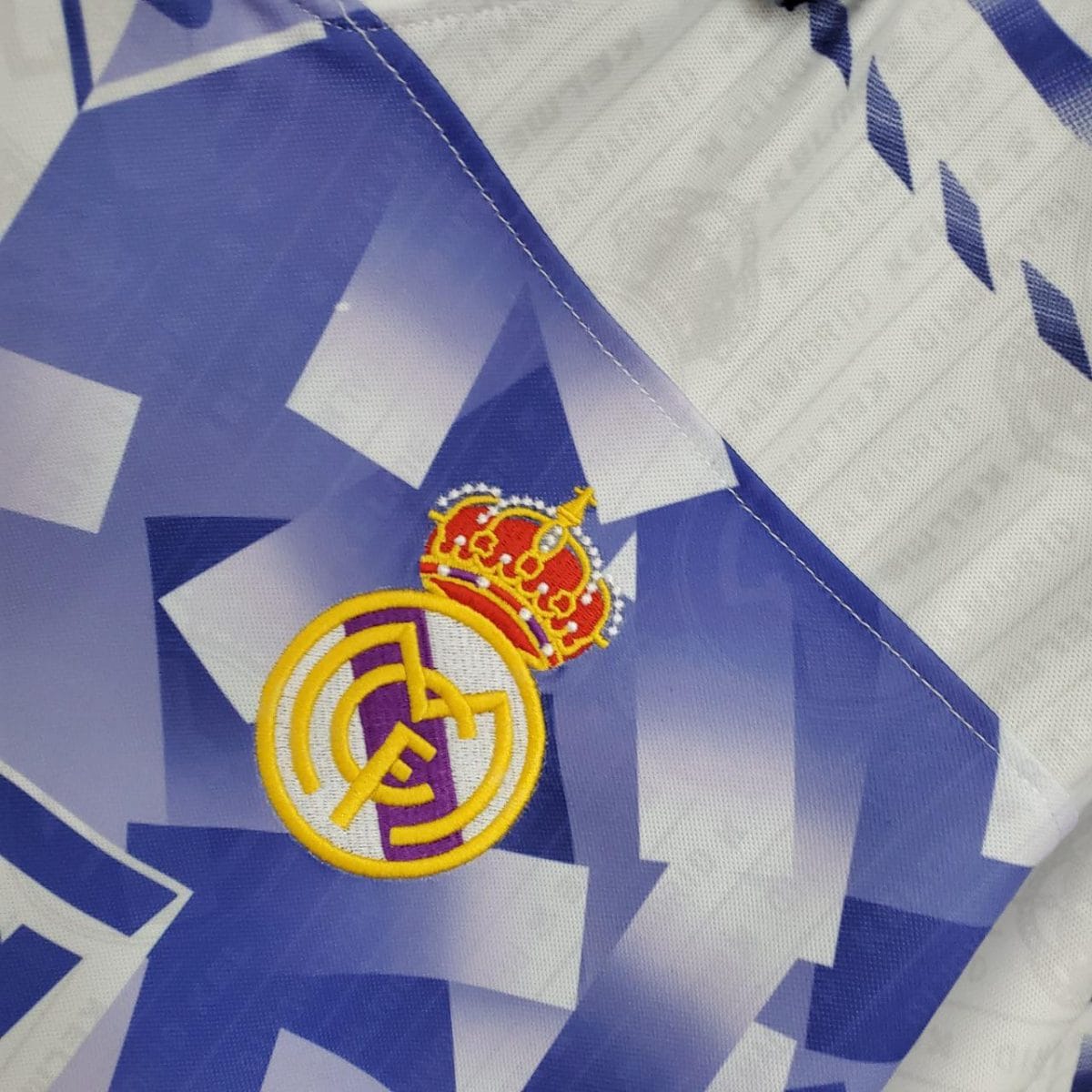 Close-up of the Real Madrid crest embroidered on blue geometric fabric background.