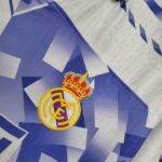 Close-up of the Real Madrid crest embroidered on blue geometric fabric background.