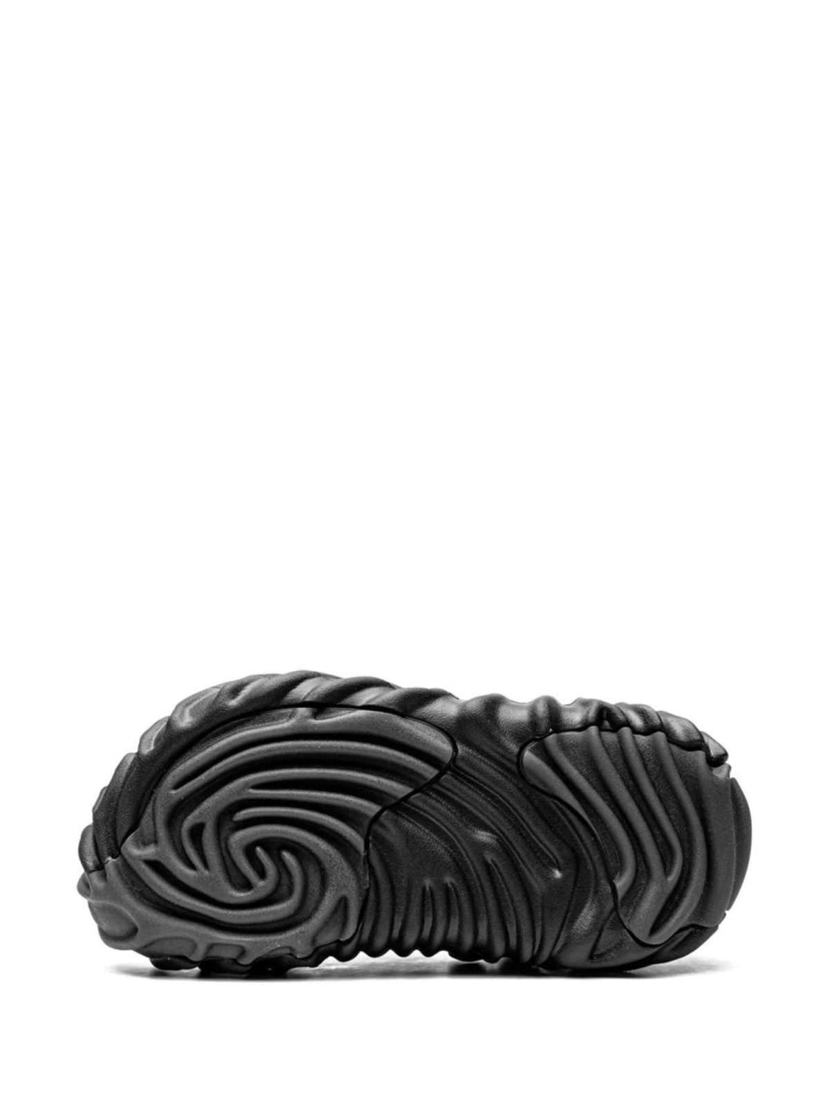 Close-up of a black sneaker sole with curved, ribbed tread patterns on a white background