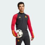 Athlete wearing a black and red jersey holds a white soccer ball against a pale background in a posed portrait.