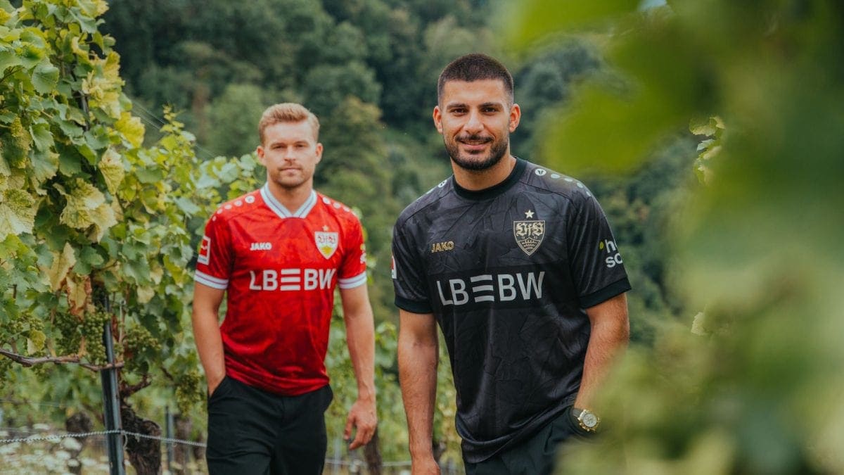 Two men in red and black soccer jerseys stand in a vineyard, posing and smiling toward the camera.