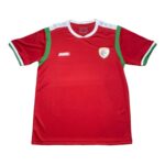Red sports jersey with white collar and green shoulder trims, featuring a badge on the left chest and a JAKO logo on the right.