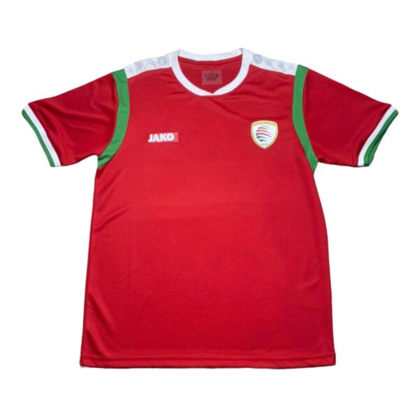 Red sports jersey with white collar and green shoulder trims, featuring a badge on the left chest and a JAKO logo on the right.