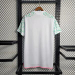 White T-shirt with mint green geometric sleeves, pink trim at hem, hanging on a wooden hanger against a metal grid shelf (informative).