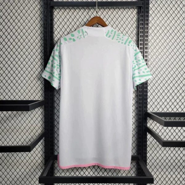 White T-shirt with mint green geometric sleeves, pink trim at hem, hanging on a wooden hanger against a metal grid shelf (informative).
