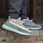 Person wearing gray knit sneakers with a pale yellow side stripe, standing on brick steps.