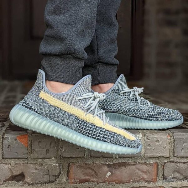 Person wearing gray knit sneakers with a pale yellow side stripe, standing on brick steps.