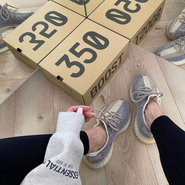 Person tying gray knit sneakers on a wooden floor, with beige boxes labeled 350 and BOOST nearby.
