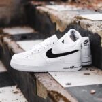 White Nike Air Force 1 sneakers resting on weathered concrete stairs with a black swoosh logo visible on the side.