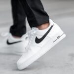 White Nike Air Force 1 sneakers with a black swoosh, mid-step on a gray surface.