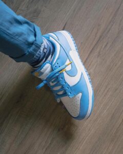 Blue and white sneakers with matching laces worn with jeans on a wood floor.