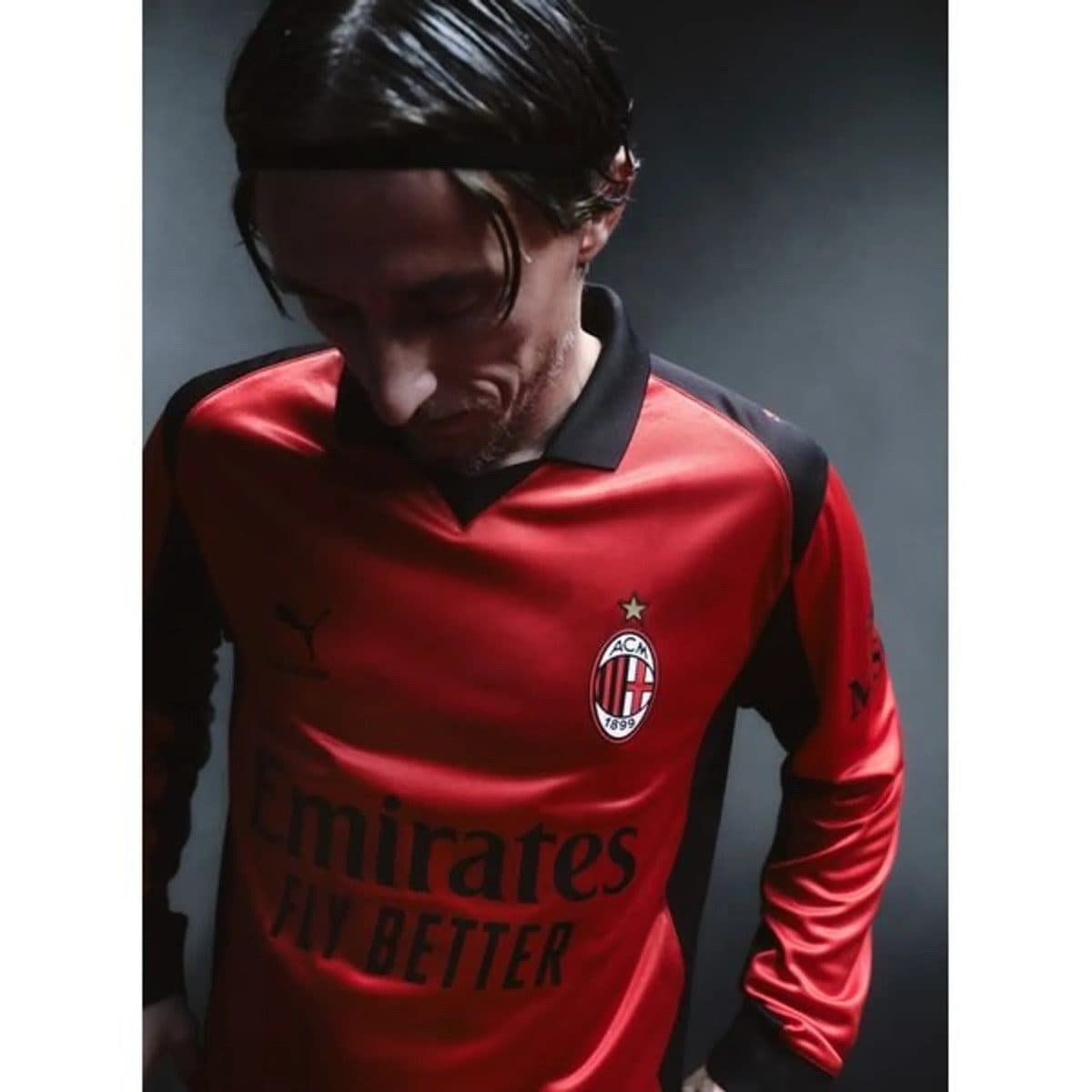 Soccer player in a red AC Milan jersey looking down, with the club crest and star visible on the chest.