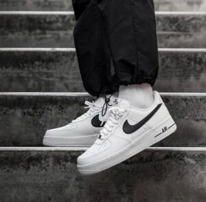Close-up of white Nike Air sneakers with a black swoosh, worn with white socks on concrete stairs.