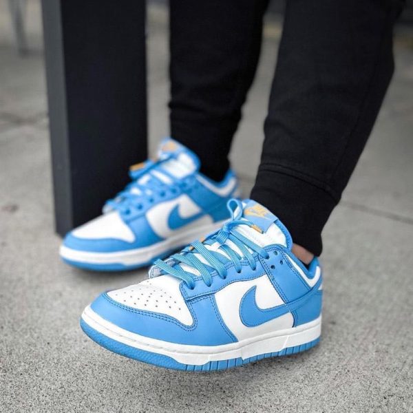 Pair of blue and white Nike sneakers on a gray sidewalk, laces tied, wearing black pants nearby.