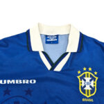 Blue Brazil national team jersey close-up showing white collar, Umbro branding, and the CBF crest with a yellow shield and blue background.