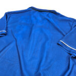 Back view of a blue polo shirt with white trim on the sleeve cuffs