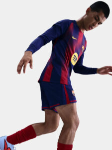 19_bed67658-8b0a-4380-81c5-88583347d8bd | UAE SPORT STORE Athlete wearing FC Barcelona jersey running forward in a diagonal pose in a light backdrop.