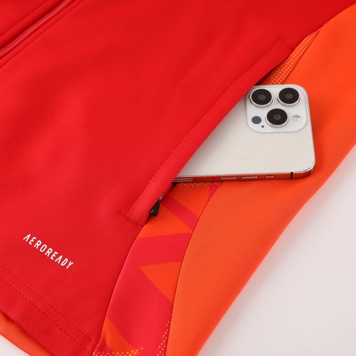 Close-up of bright red fabric with diagonal seam lines and a corner of a smartphone showing a three-camera array peeking from the bottom right.