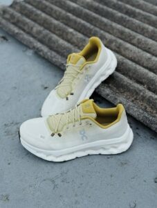 Pair of white On running shoes with pale-yellow lining resting on concrete steps, angled for a streetwear look.