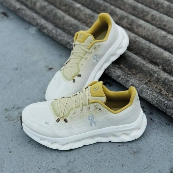 Pair of white On running shoes with pale-yellow lining resting on concrete steps, angled for a streetwear look.