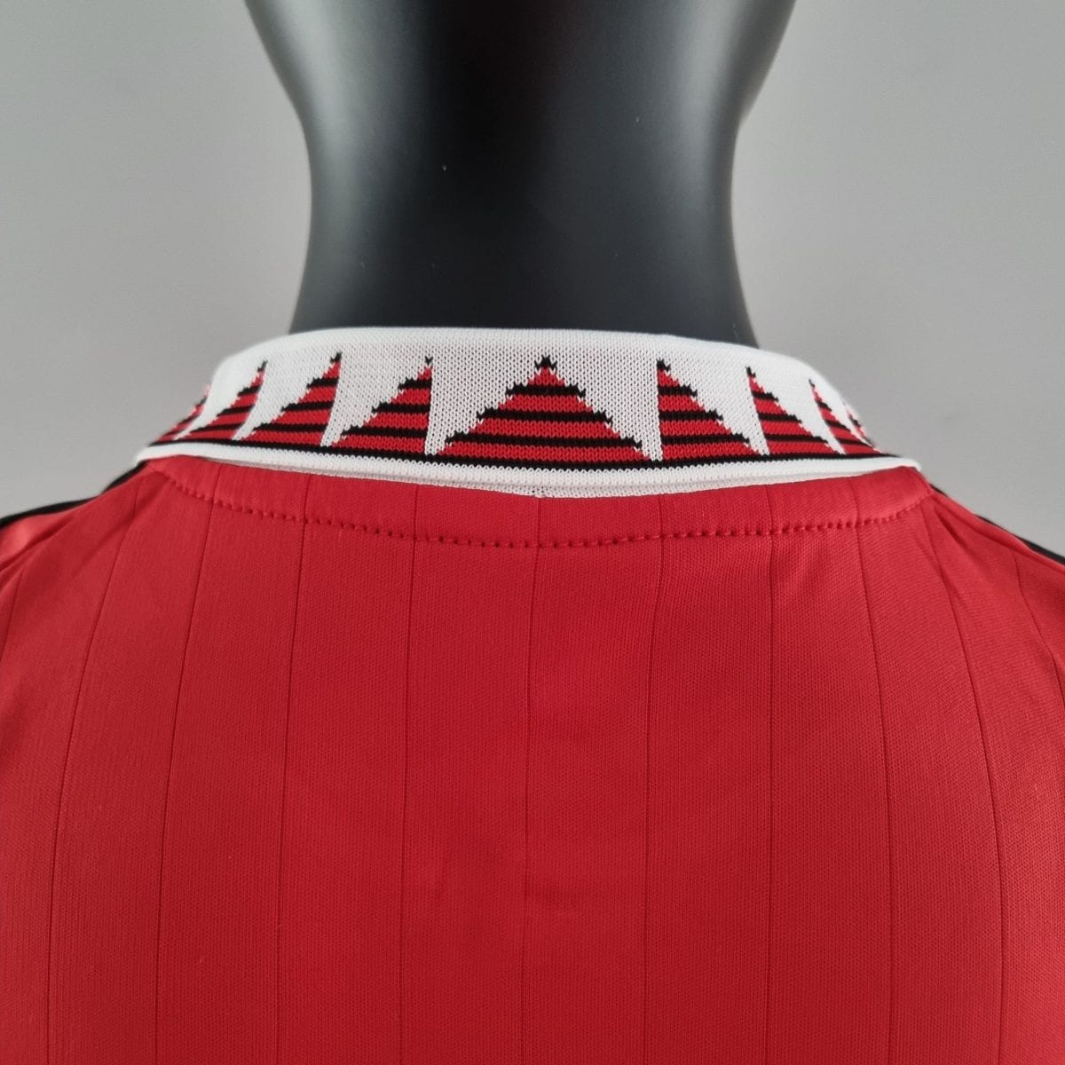 Back view of a black mannequin wearing a red knit shirt with a white collar featuring red triangular patterns.
