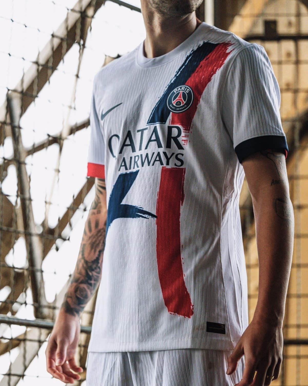 Person wearing a white Paris Saint-Germain jersey with the Qatar Airways sponsor and bold red-blue brushstroke graphics.